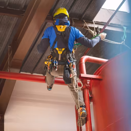een monteur hangt met touwen aan een draagbalk en voert onderhoud uit